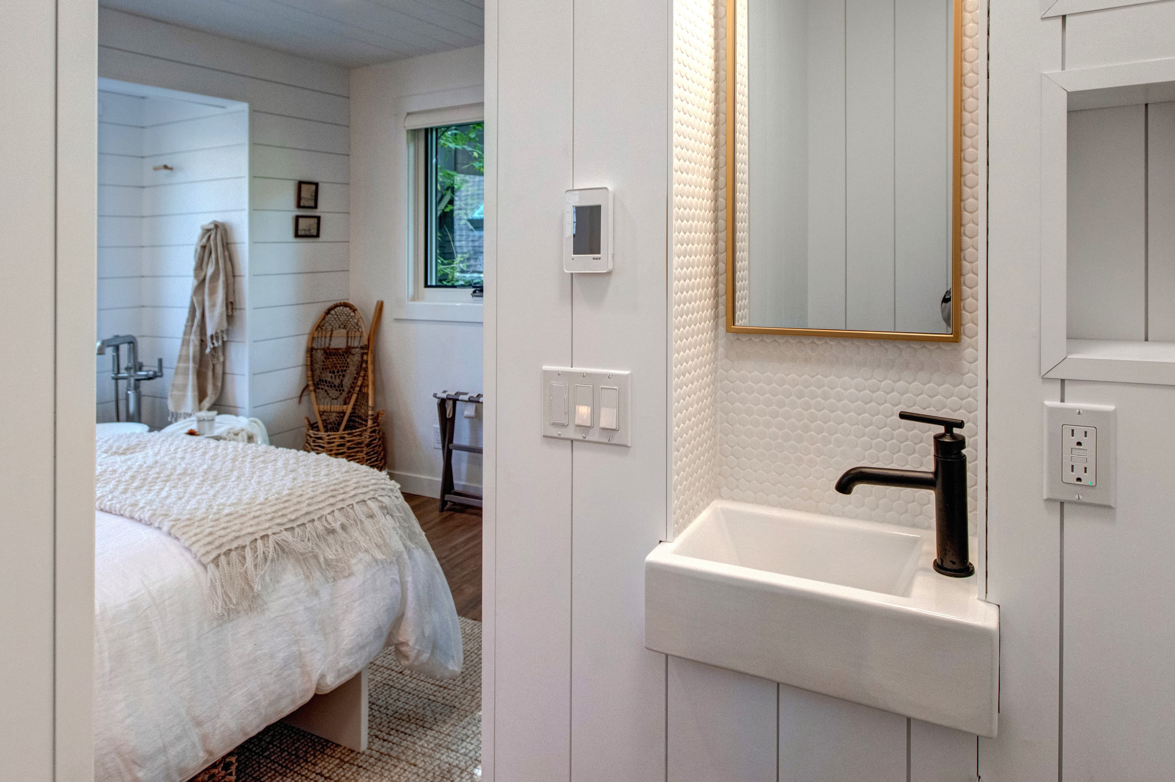 Lofted bedroom in detached guest suite, with a queen bed next to standalone bathtub and half bathroom.