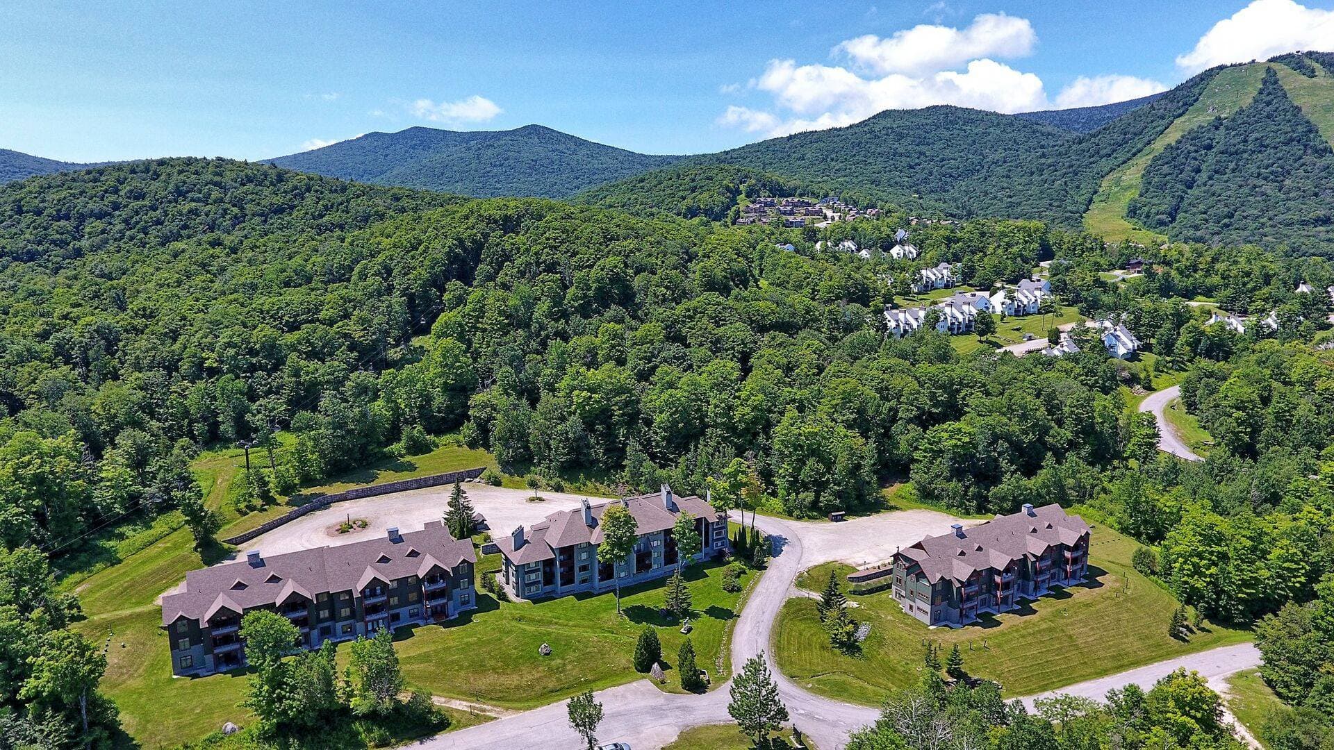 Aerial view of The Lodges surrounded by lush green mountains. The complex features outdoor pool access, scenic walking trails, and breathtaking views in every direction.
