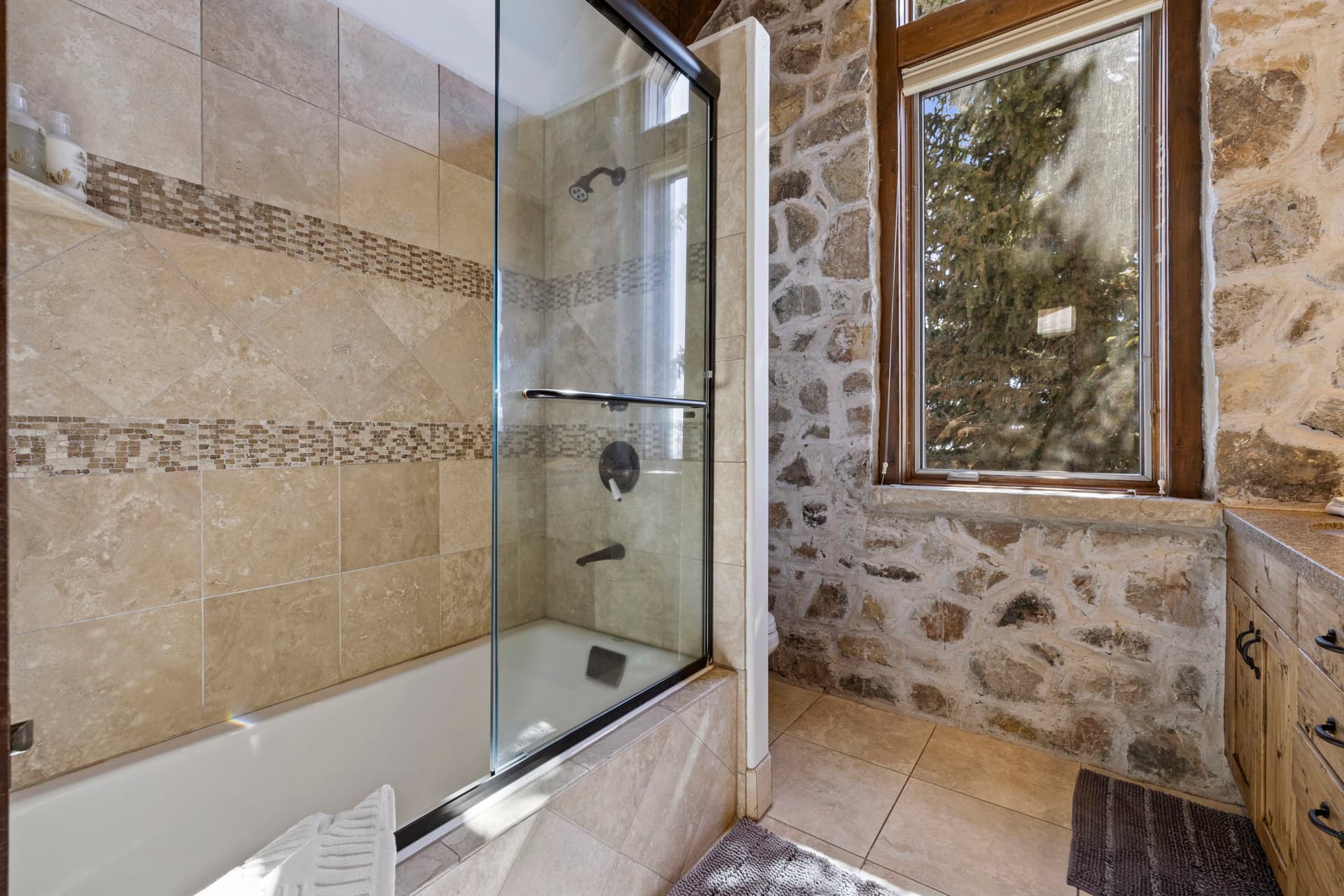 Bathroom with glass-enclosed shower, stone walls, and window with natural light.