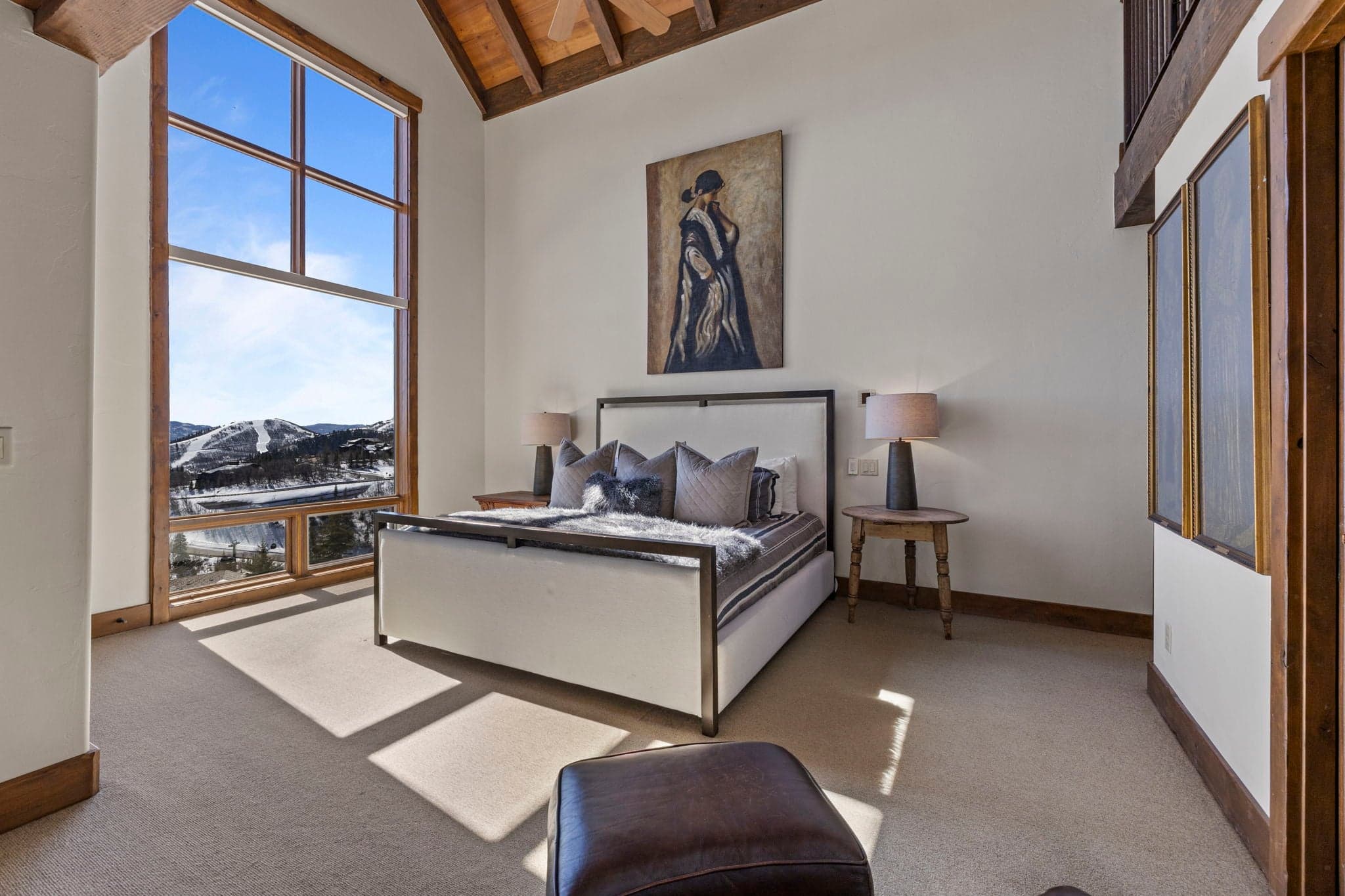 Bedroom with upholstered bed, vaulted ceilings, and mountain views through tall windows.