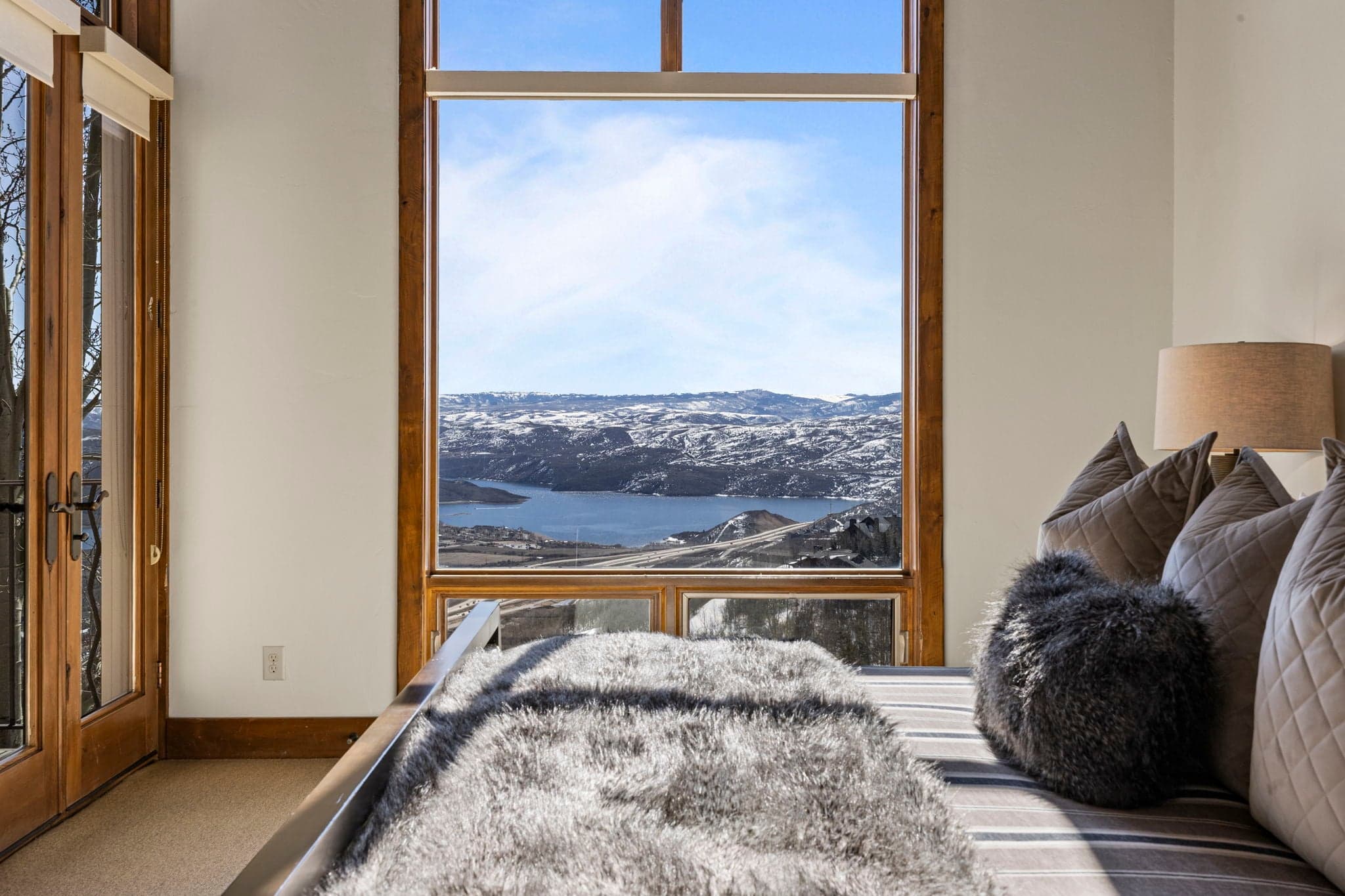 Grand primary suite with expansive windows overlooking the lake and snow-covered mountains.