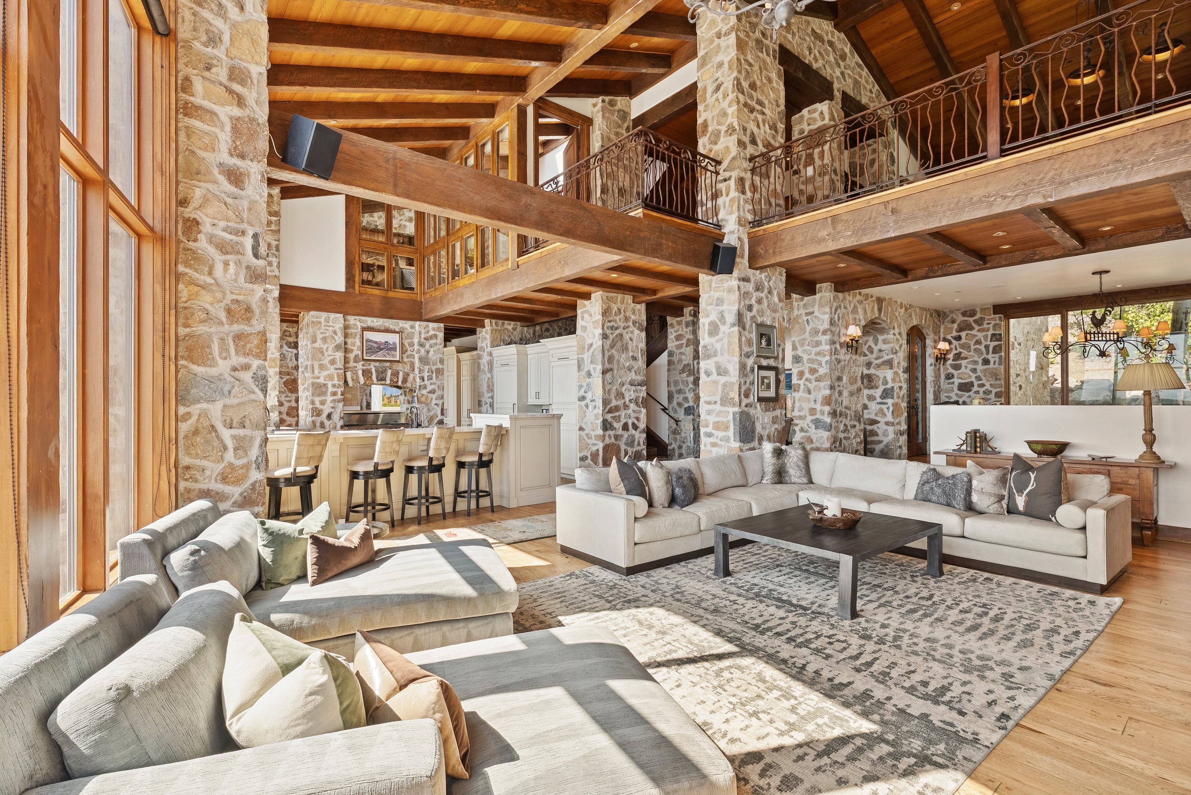 Open-concept living and dining area with sectional sofa, stone walls, and rustic chandelier.