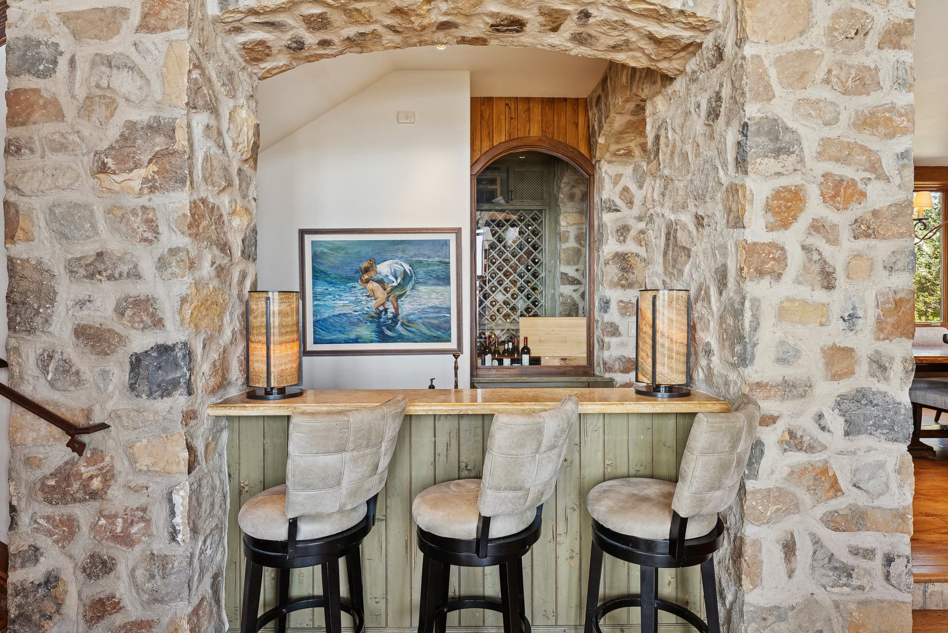 Stone bar with upholstered stools and built-in wine storage.