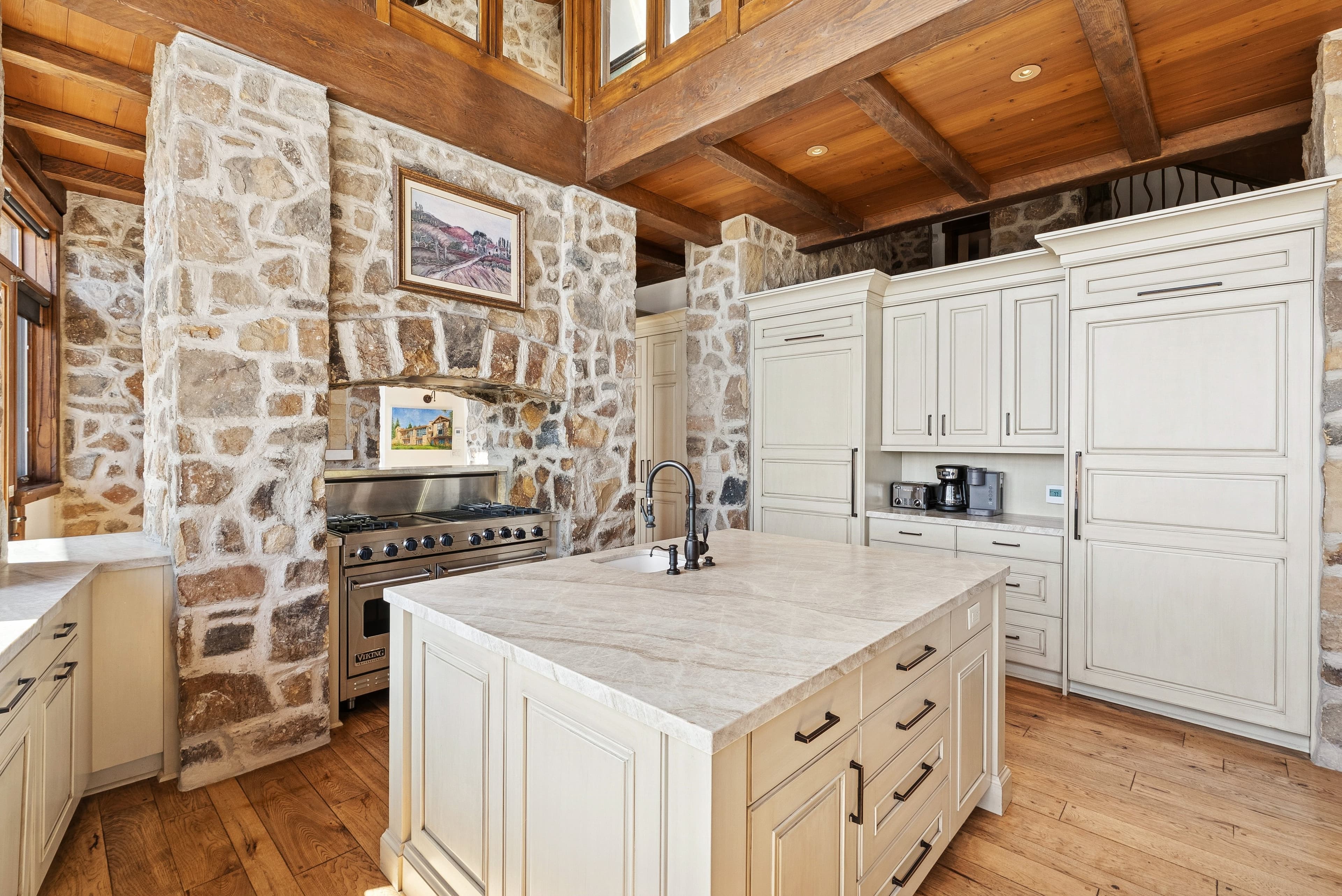 Kitchen with marble island, farmhouse sink, and stone walls under vaulted wood ceilings