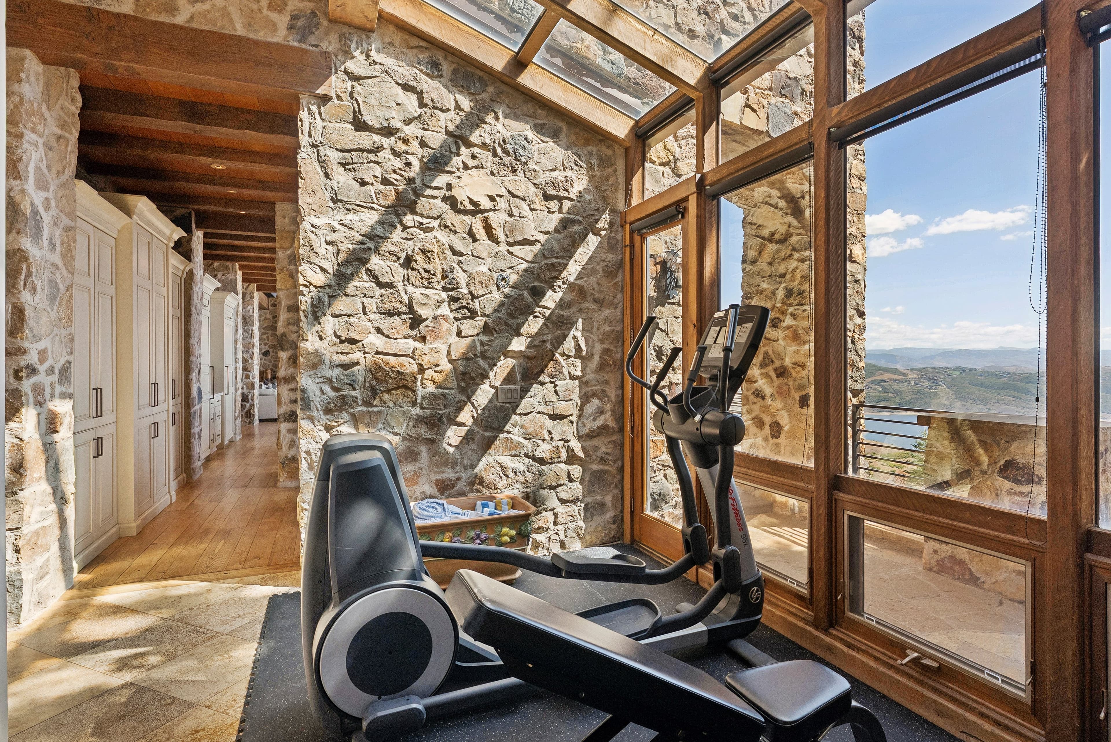 Home gym with exercise equipment in a glass-enclosed room overlooking mountain views.