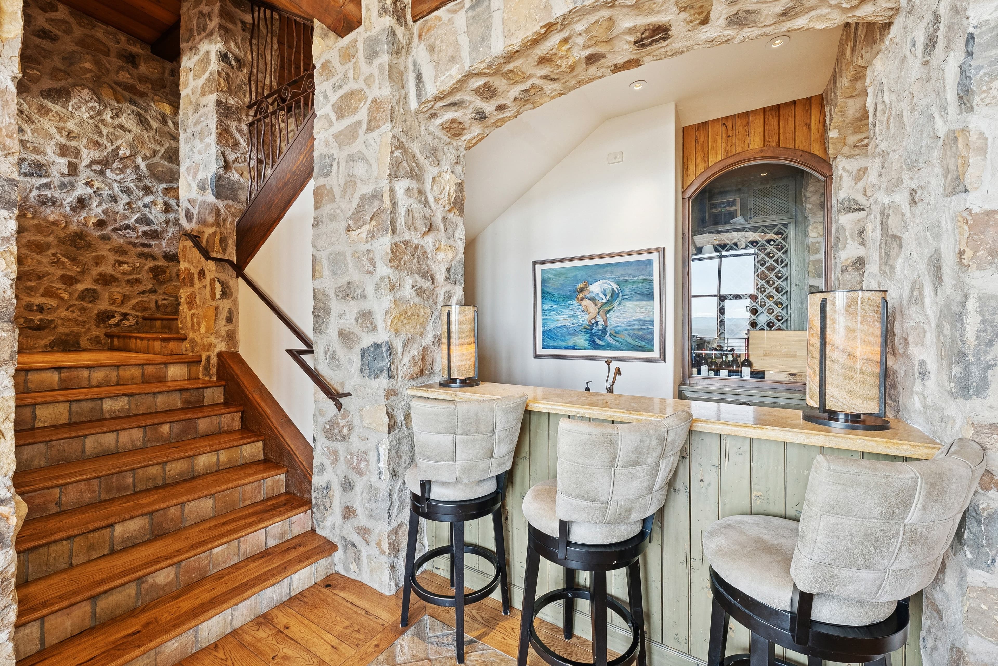 Stone bar area with upholstered stools and rustic details inside a mountain retreat.