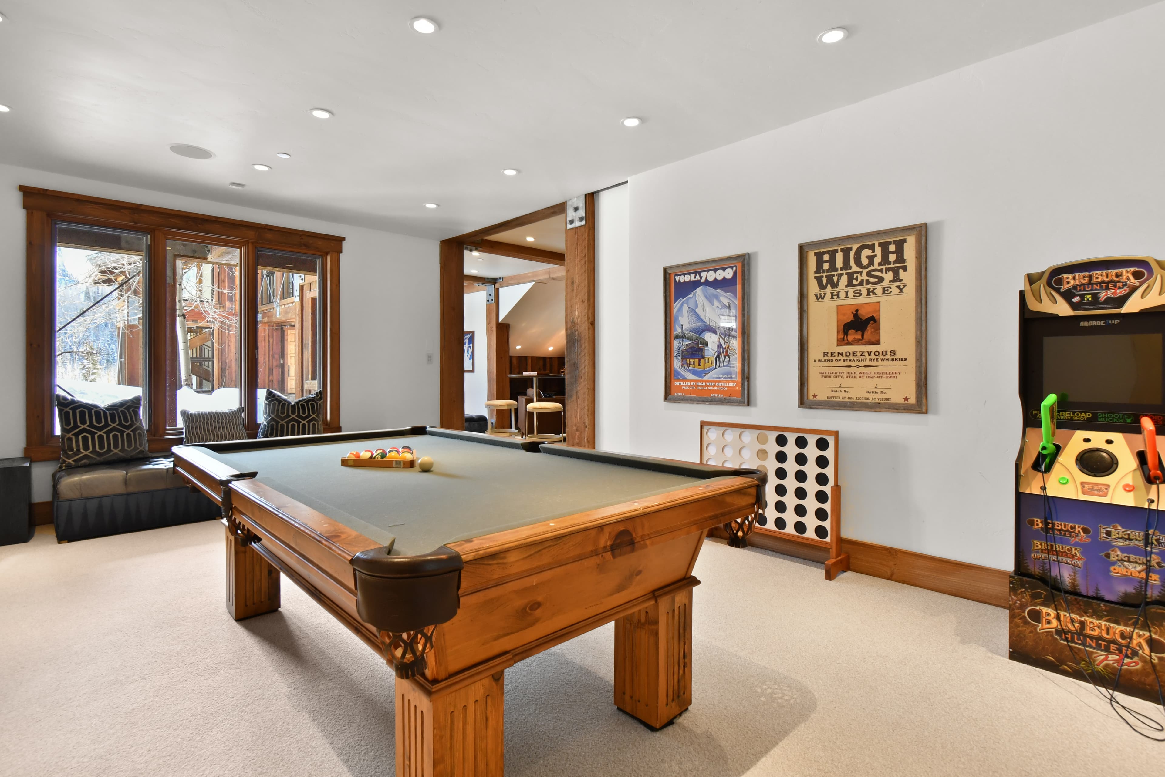 A pool table sits in the center of the game room of Talus Ridge, next to an arcade cabinet and a large window.