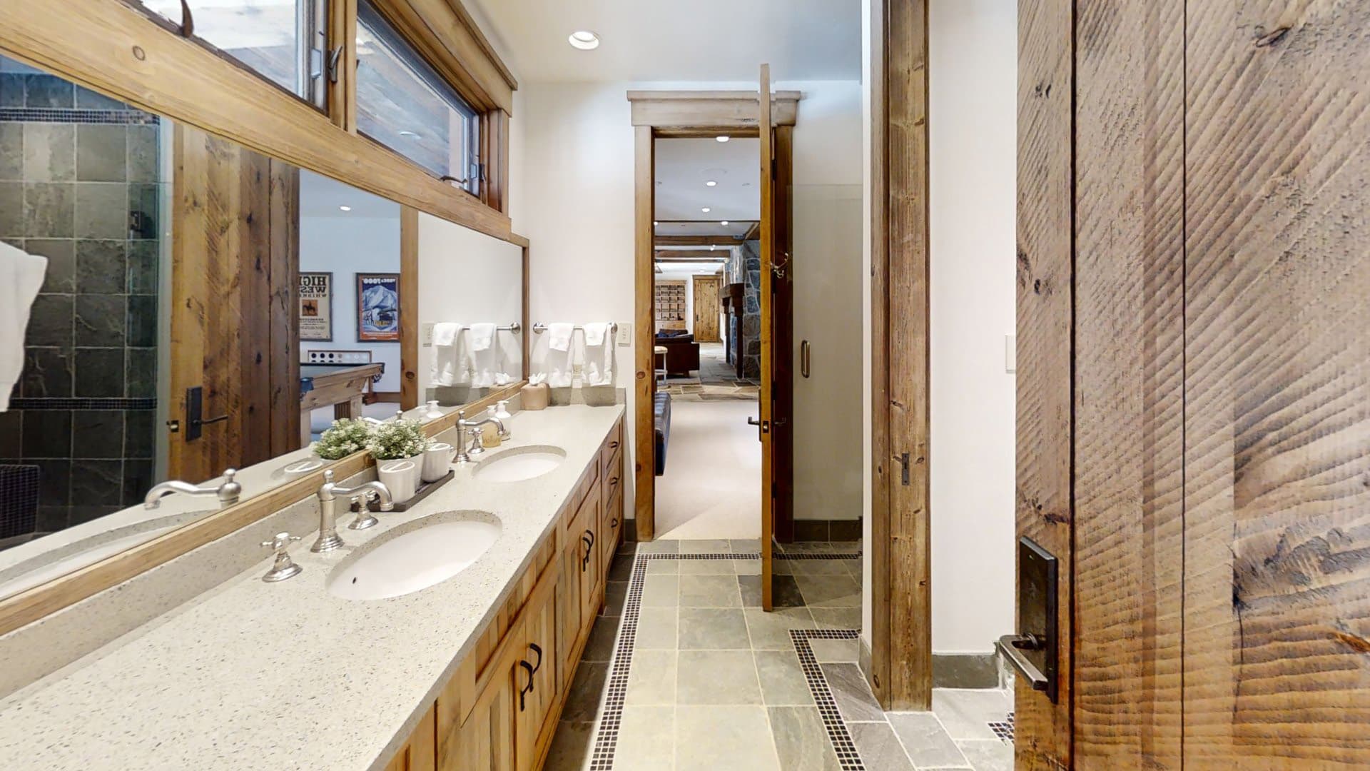 A look at the bathroom of the home, with a jack and jill sink in front of a large mirror leading to an open door.