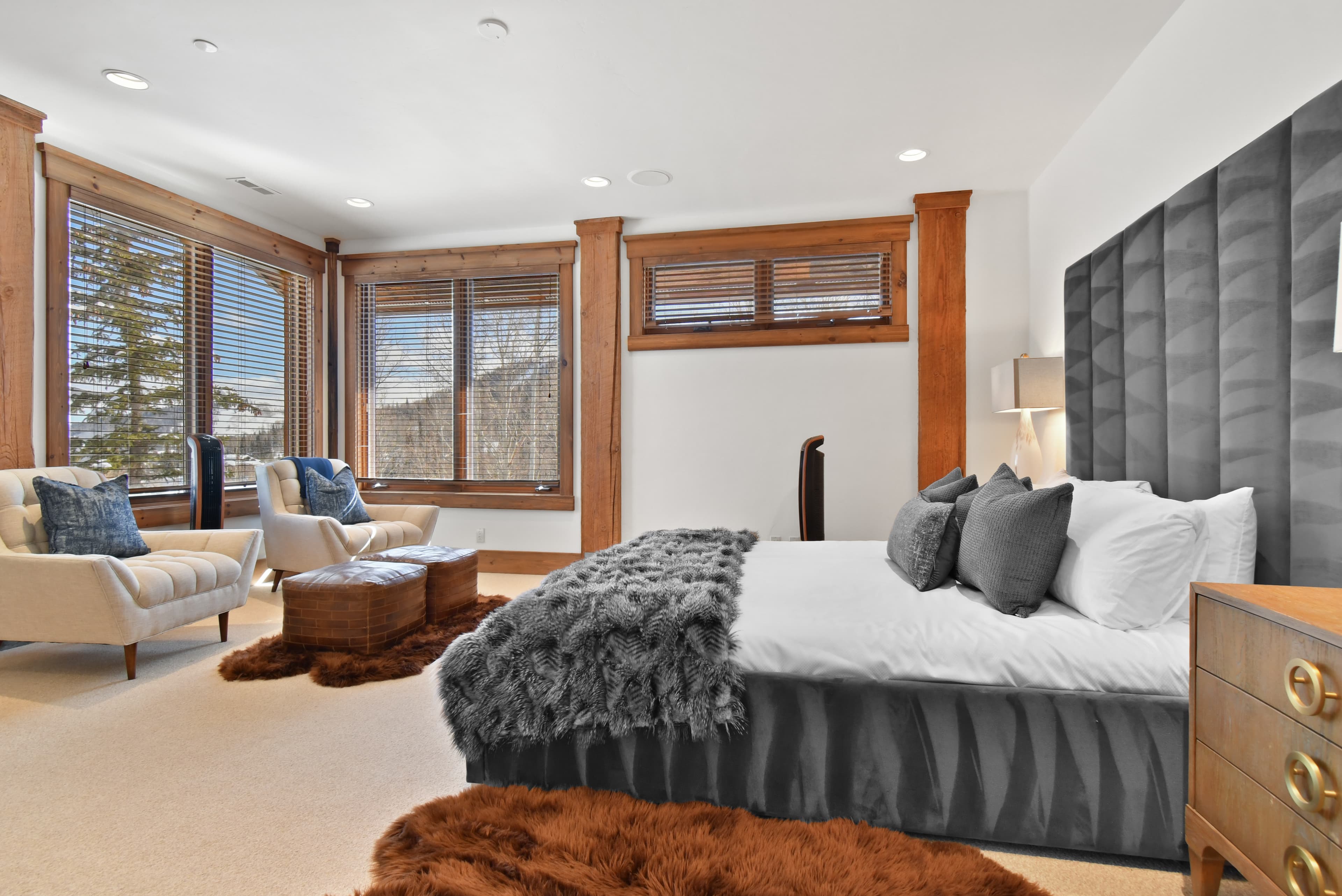 A fur blanket lays at the foot of a large bed, in front of two armchairs and ottomans.