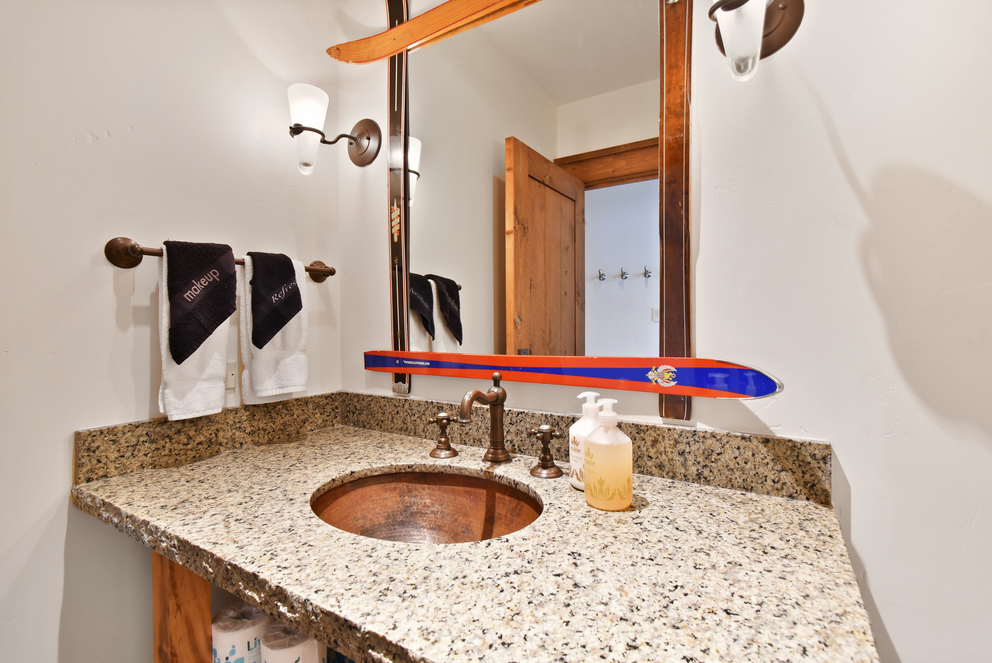 A mirror with a frame made of skis hangs above a sink.