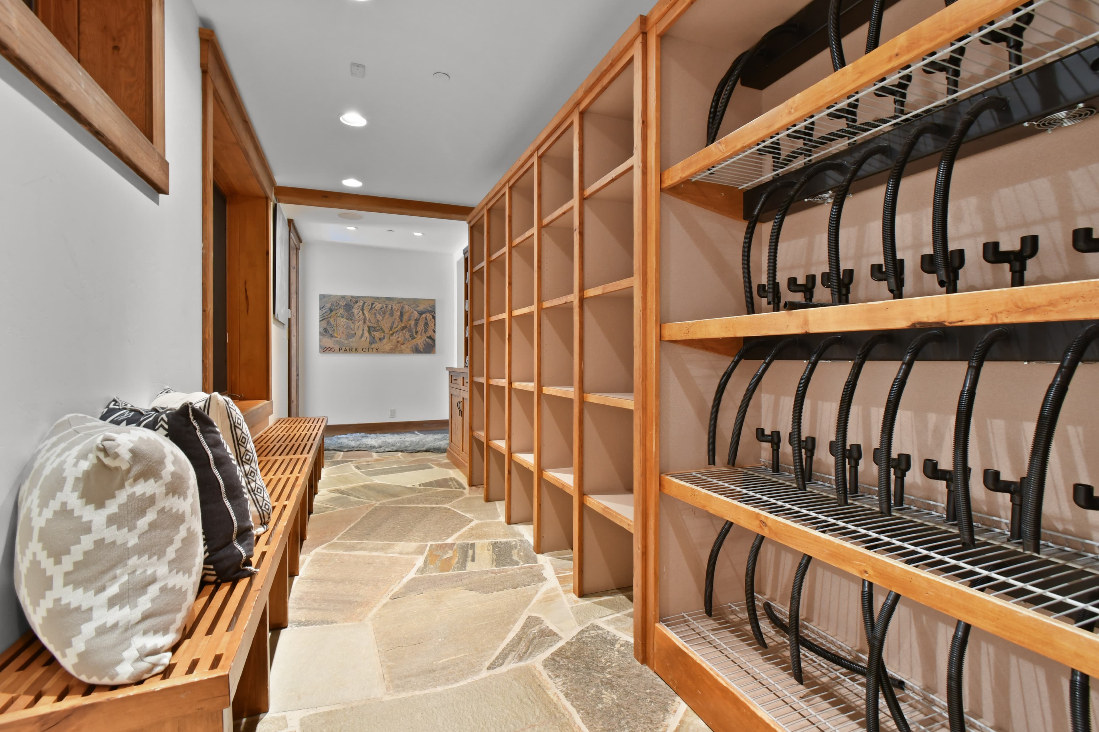 Racks and shelves line one of the walls of the ski closet, with a bench and cushions on the other wall.