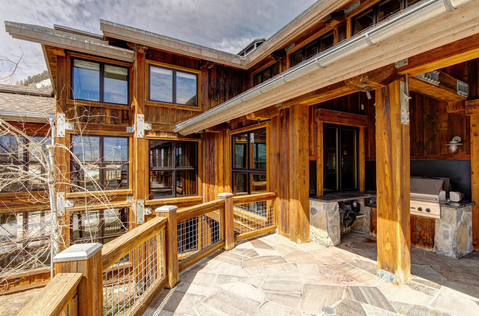 A grill lies under the roof of an outdoor patio, facing the house.