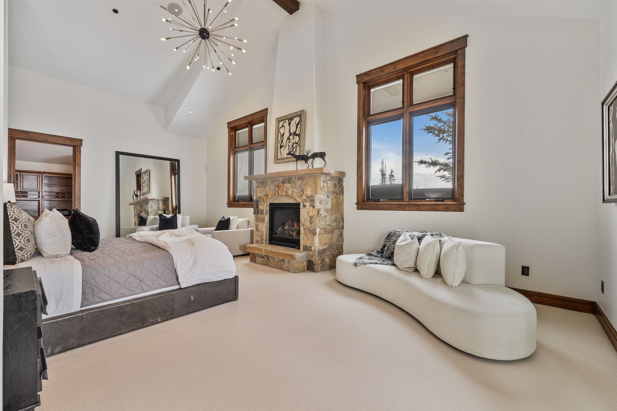 a view of the loveseat in the master bedroom with the king bed and stone fireplace and a view of the mountains