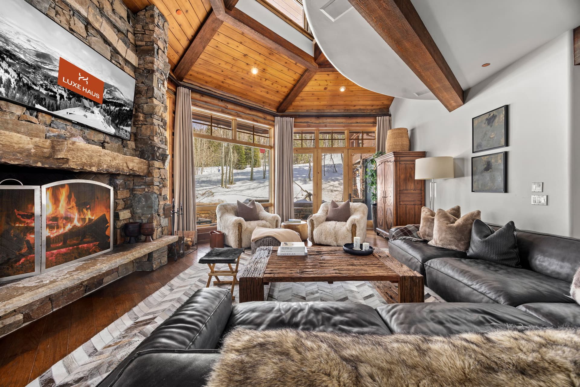 a view of the living room with large windows and views of the slopes. there is a screen saver on the TV that says Luxe Haus
