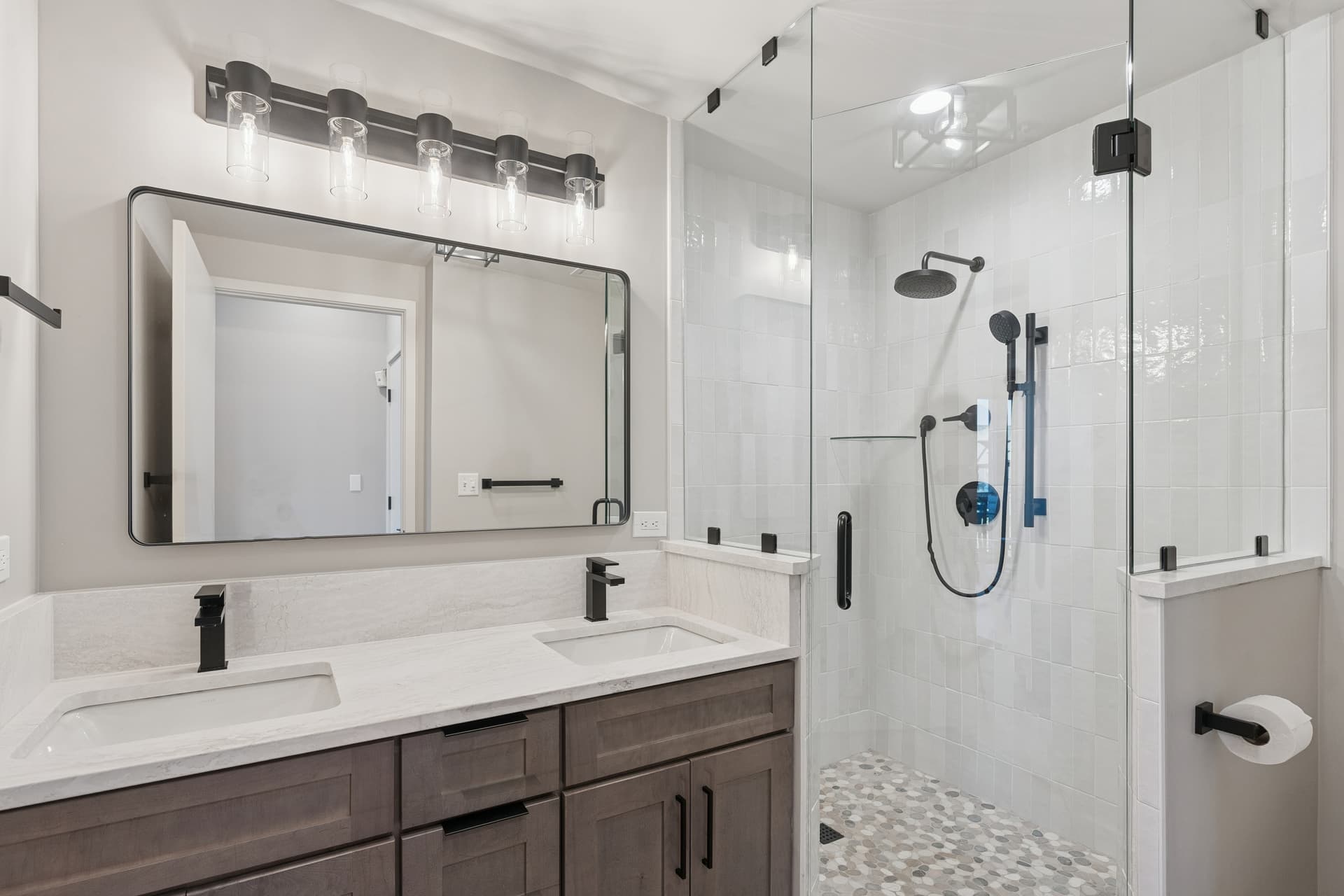 Spacious condo bathroom with double vanity, marble counters, and a walk-in glass shower.
